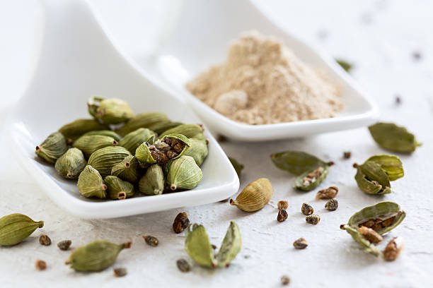 Fresh green cardamom pods and ground cardamom powder displayed on a white background, showcasing the spice in its natural and processed forms.